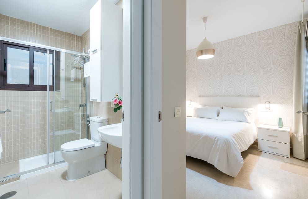 Habitación & Cuarto de Baño Interior de un apartamento donde se ve el salón a un lado y el cuarto de baño al otro, separados por un pequeño tramo de pared.